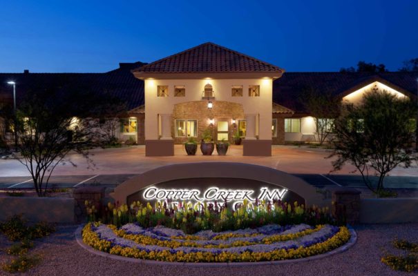 exterior nighttime view of copper cree inn memory care senior living in chandler arizona, showing the well lit sign in front of the entrance