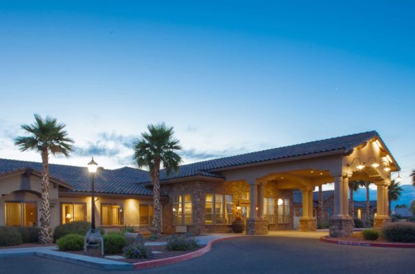 exterior sunset view of rock creek memory care in surprise arizona, showing landscaping dotted by palm trees and mountains in the distance